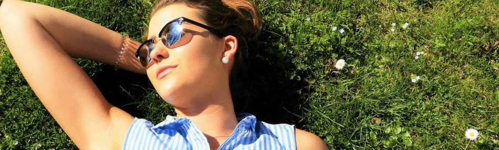 Girl laying in grass with sunglasses looking into the sun