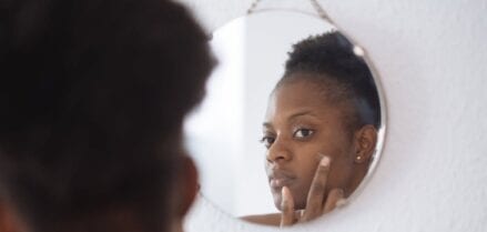 Girl looking in mirror applying cream to skin.