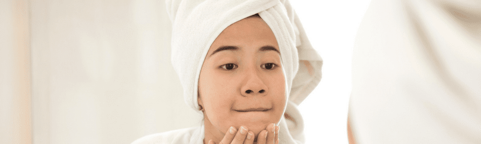 Woman wearing a towel on her head and looking at skin in the mirror