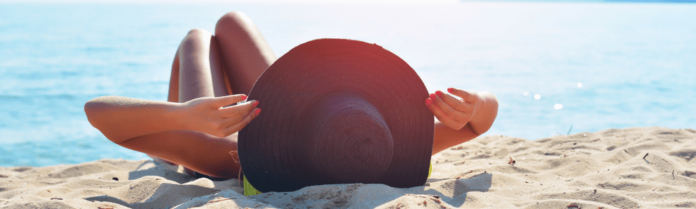 Woman laying on the sand on the beach wearing a big sun hat