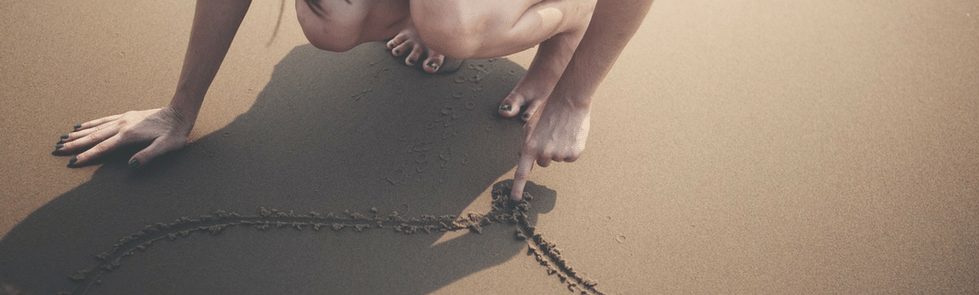 Woman drawing a heart in the sand at the beach
