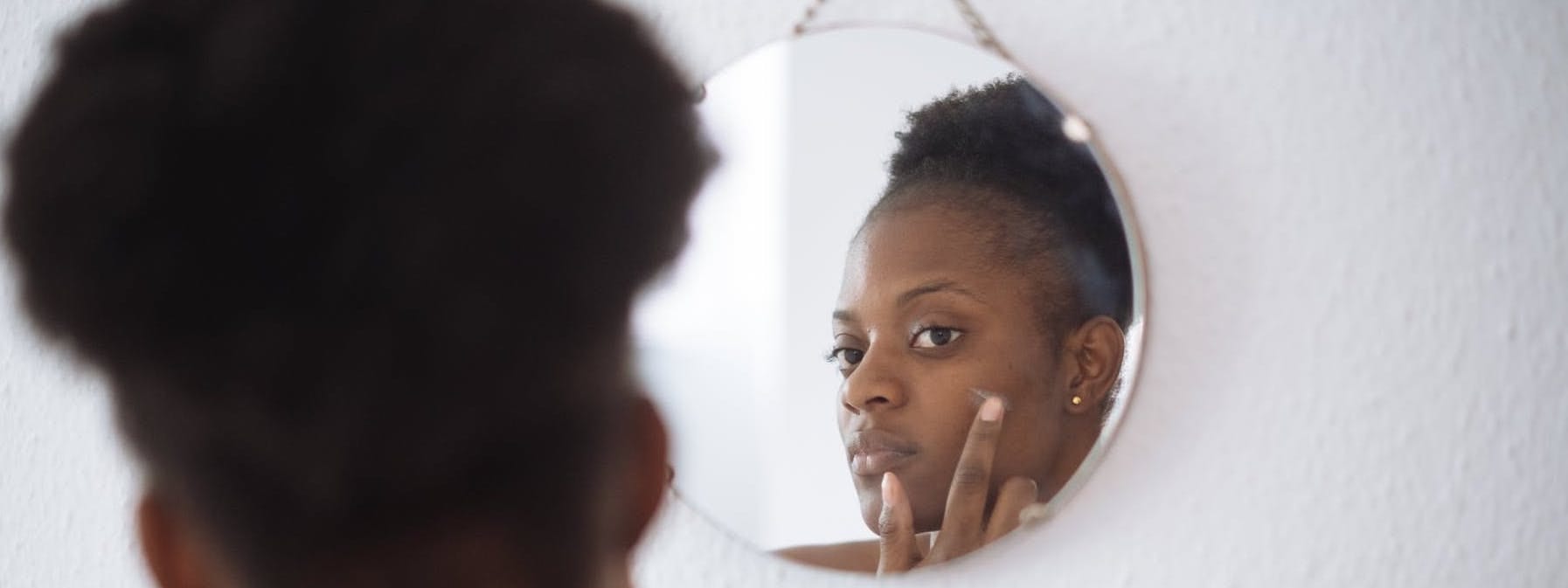 Woman applying skincare while looking in the mirror