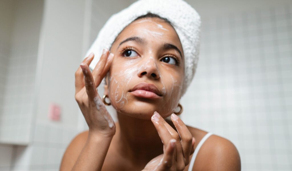 Woman looking in mirror while cleaning her face with skincare products