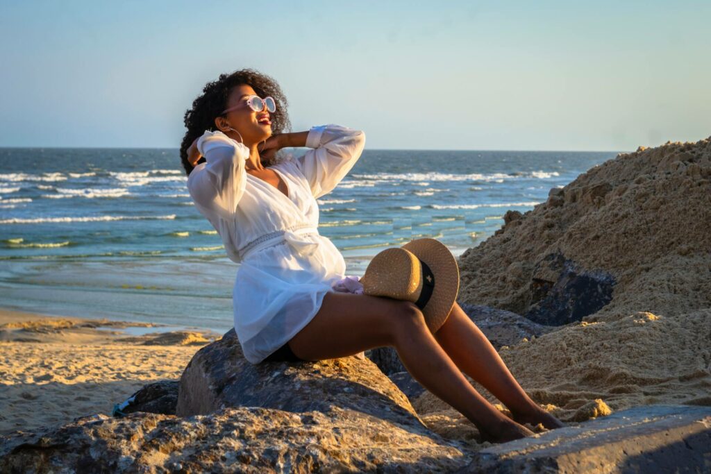 Woman in a white cover up on the beach sitting on a rock