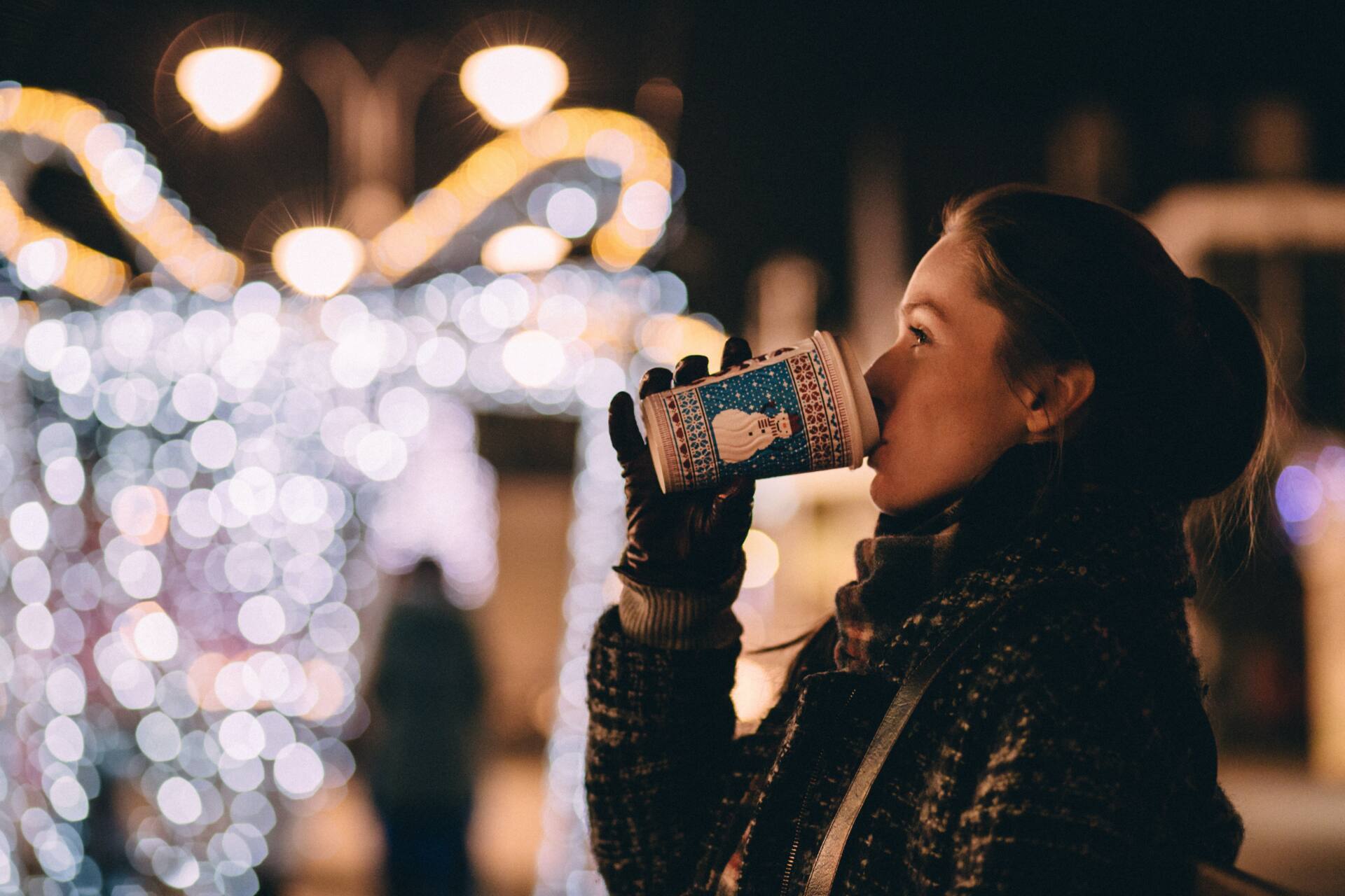 Woman drinking hot cocoa in front of holiday lights