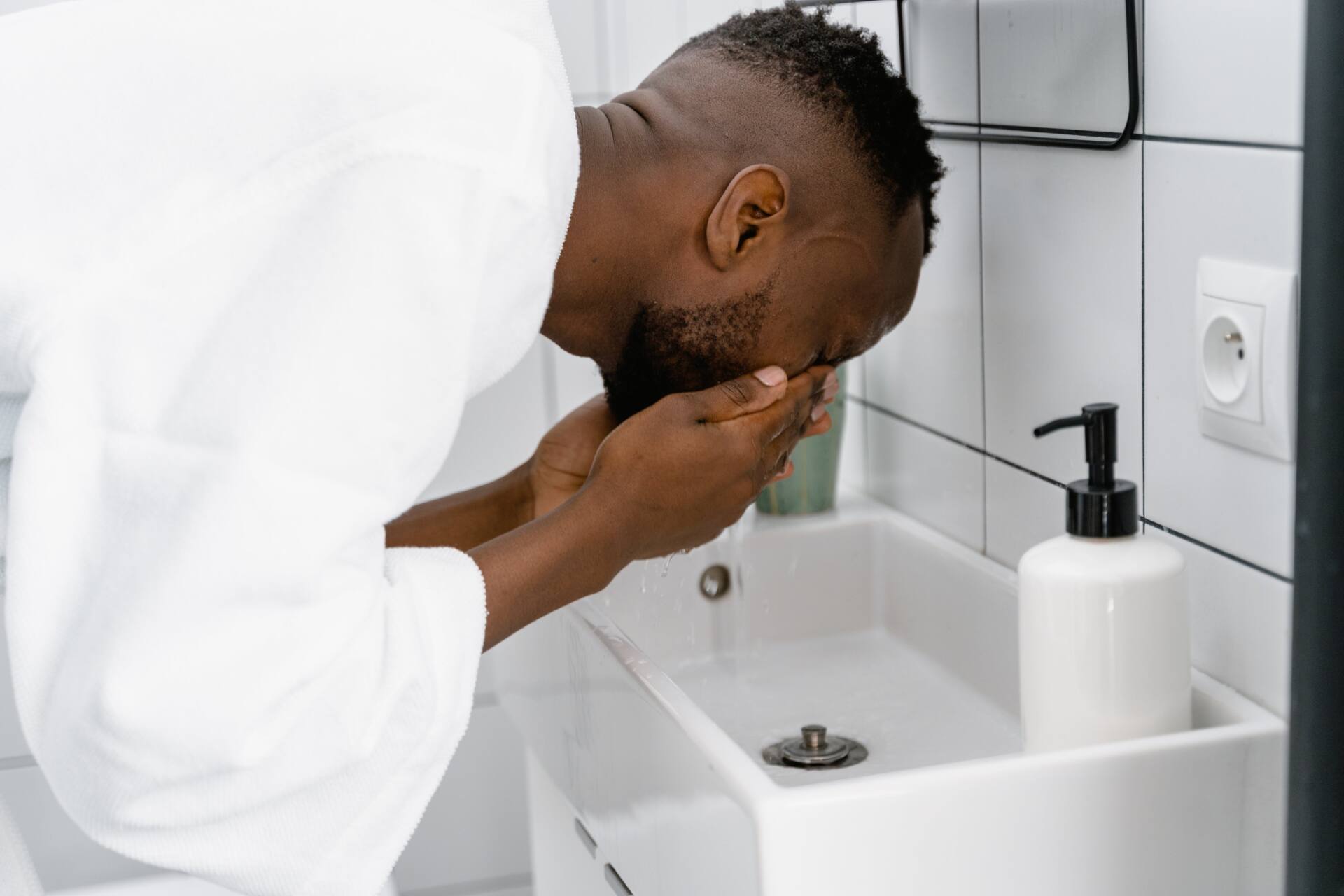 Man wearing white bathrobe and washing his face in the sink water