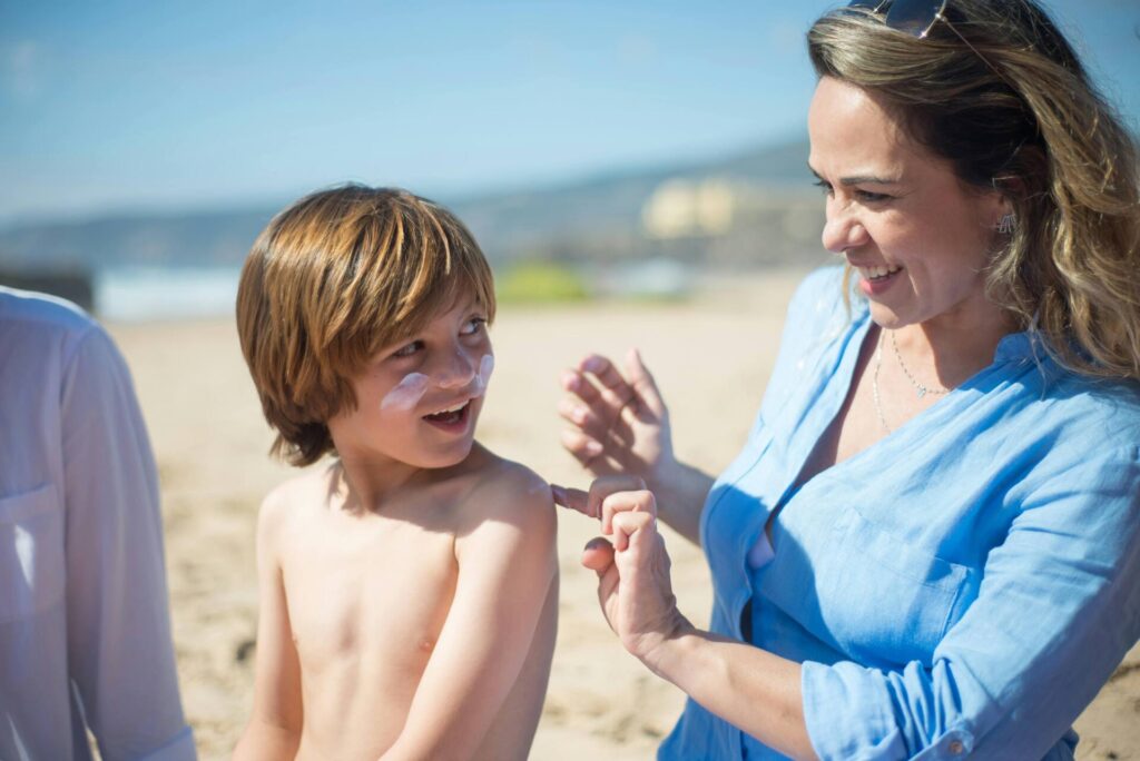 Mom applying sunscreen to boy at the beach