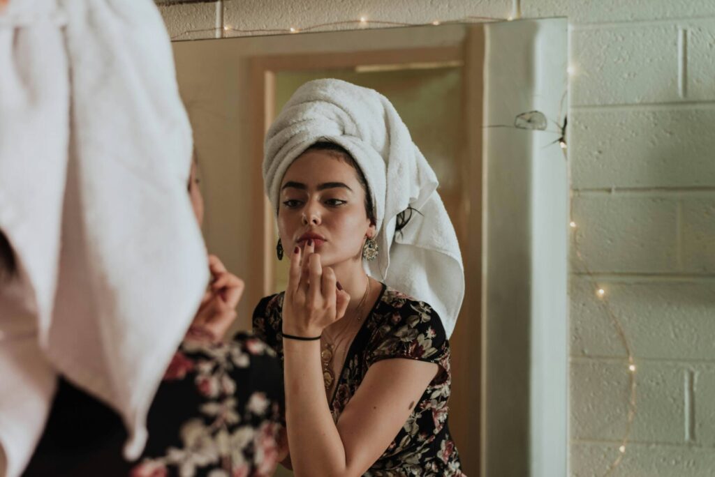 Woman with towel on head looking in the mirror while doing skincare