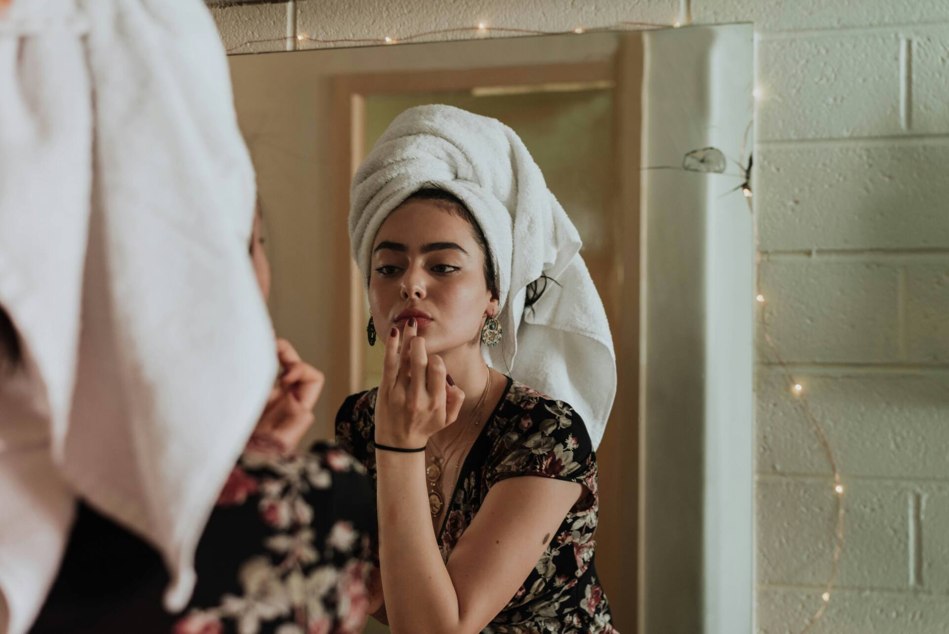 Woman with towel on head looking in the mirror while doing skincare