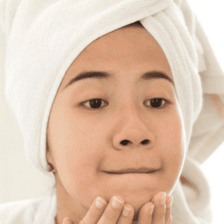 Woman wearing a towel on her head and looking at skin in the mirror
