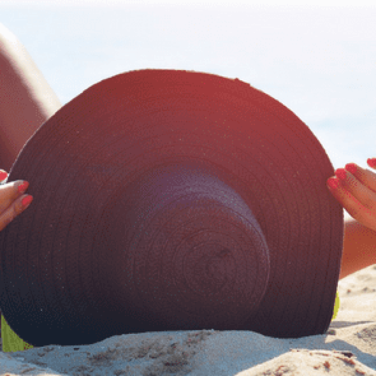 Woman laying on the sand on the beach wearing a big sun hat