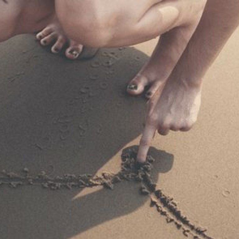Woman drawing a heart in the sand at the beach