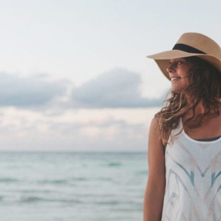 Woman wearing sun hat walking on the beach at sunset