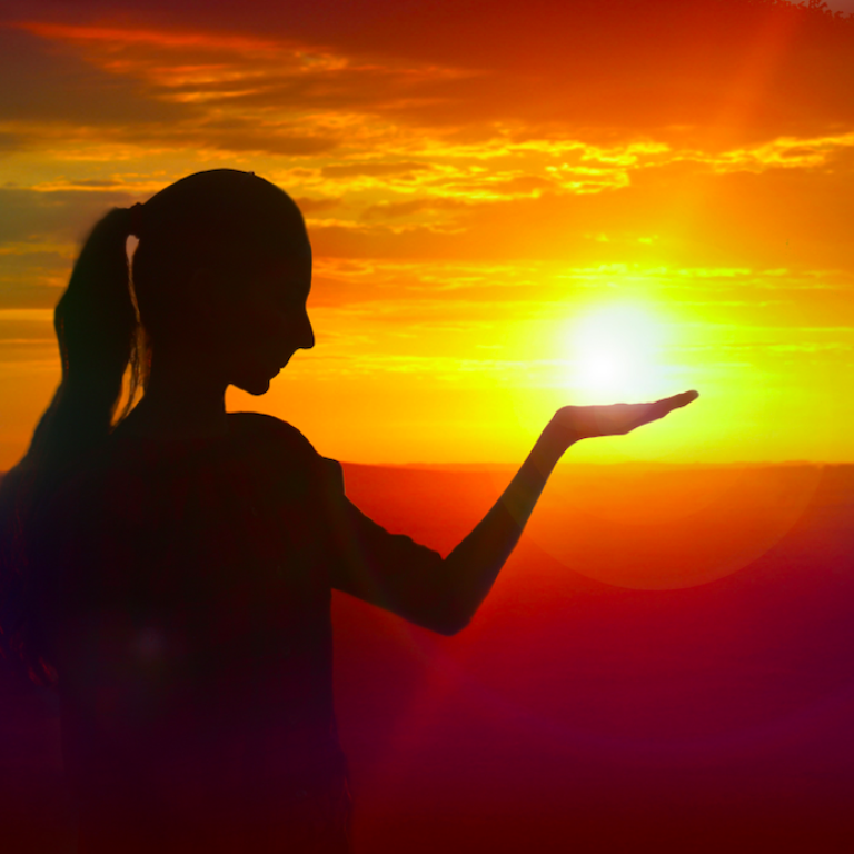 Woman pretending to hold the sunset in her hands