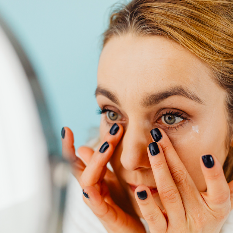 Woman looking at under eyes in a mirror