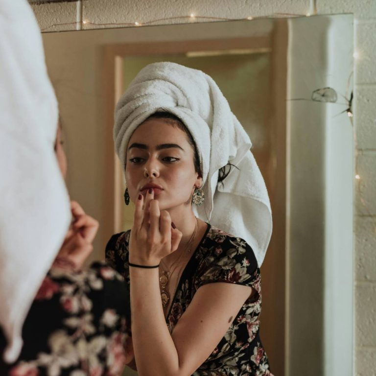 Woman with towel on head looking in the mirror while doing skincare
