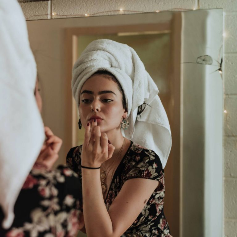 Women with hair wrapped in a towel looking in the mirror and touching lips
