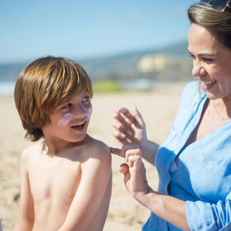 Mom applying sunscreen to boy at the beach