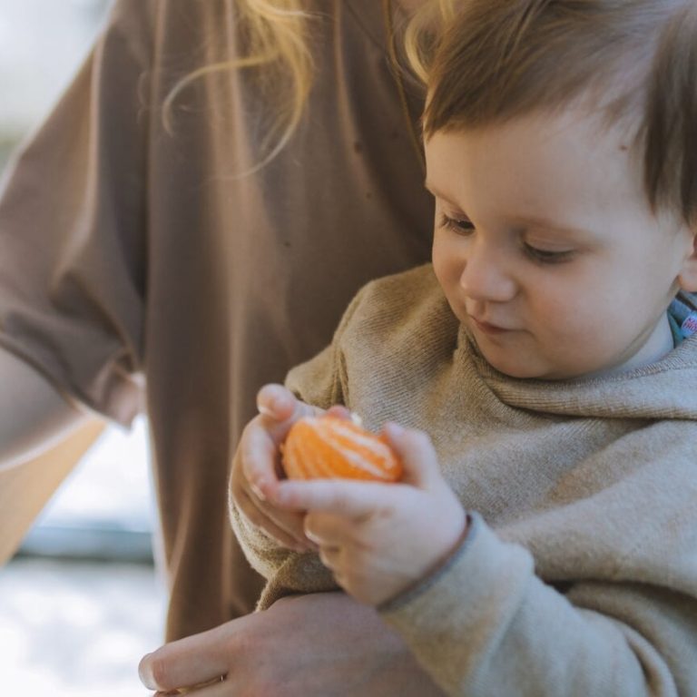 Little boy sitting in mom's lap eating an orange