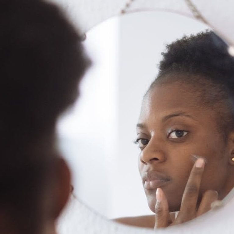 Woman applying skincare while looking in the mirror