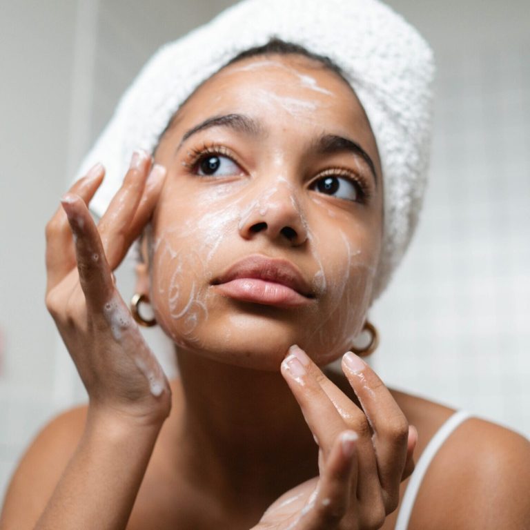 Woman looking in mirror while cleaning her face with skincare products
