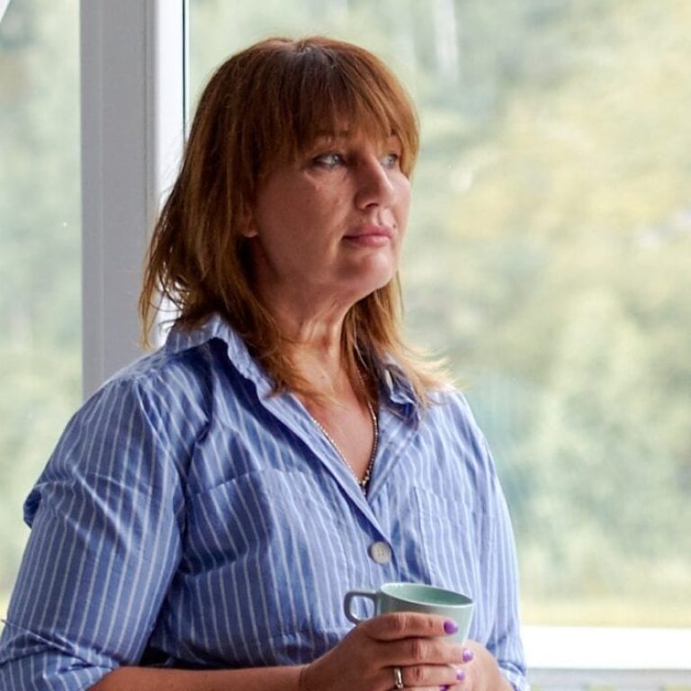 Older woman holding a coffee mug staring out a window