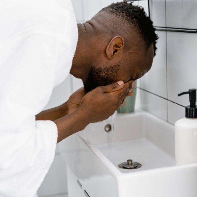 Man wearing white bathrobe and washing his face in the sink water