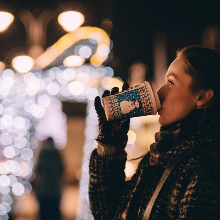 Woman drinking hot cocoa in front of holiday lights